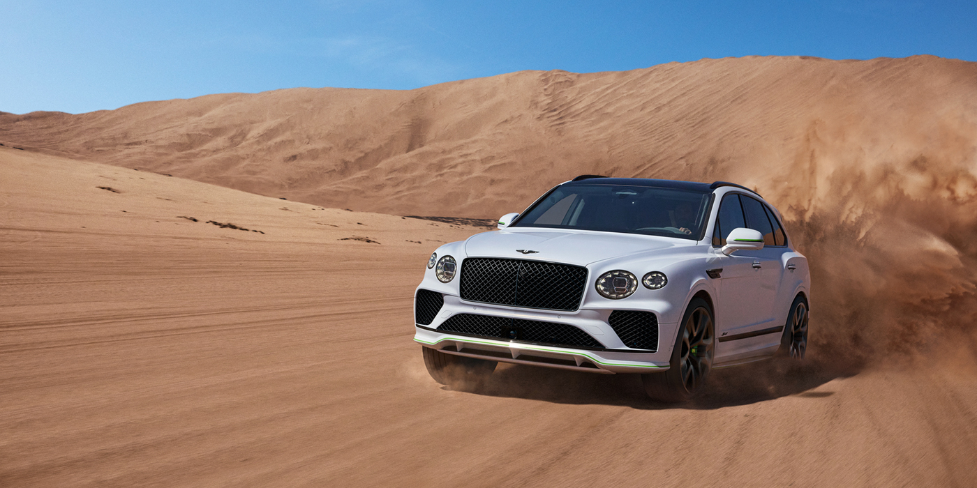 Bentley Stockholm Bentley Bentayga Speed SUV front three quarter in Snow Quarts Pearlescent by Mulliner white paint driving dynamically through the desert