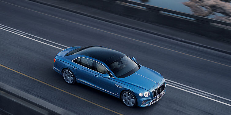 Bentley Stockholm New Bentley Flying Spur Azure sedan in Light windsor blue paint by Mulliner, with 22 inch Azure wheels seen from overhead driving dynamically on a country road