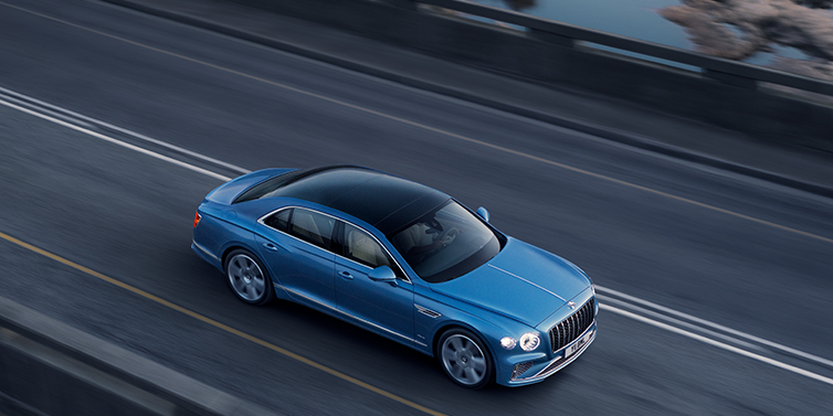 Bentley Stockholm New Bentley Flying Spur Azure sedan in Light windsor blue paint by Mulliner, with 22 inch Azure wheels seen from overhead driving dynamically on a country road