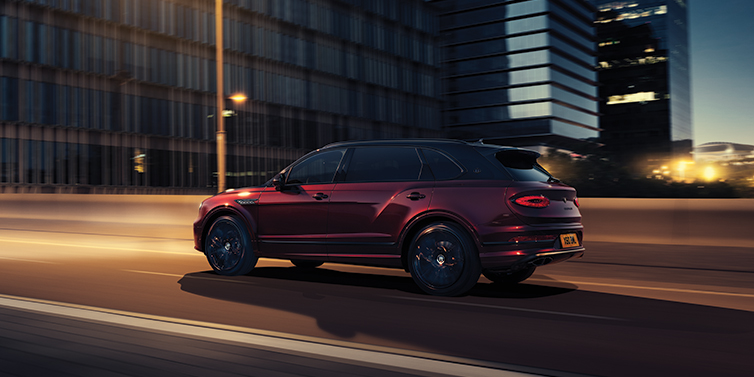 Bentley Stockholm Bentley Bentayga Extended Wheelbase Mulliner SUV in Cricket Ball red paint driving dynamically in city at night